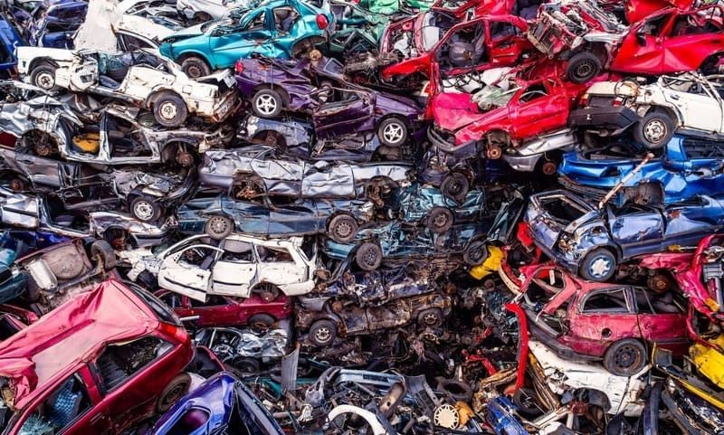 Large pile of crushed and stacked junk cars in various colors at an automotive scrapyard, representing vehicle recycling, car disposal, and auto salvage.