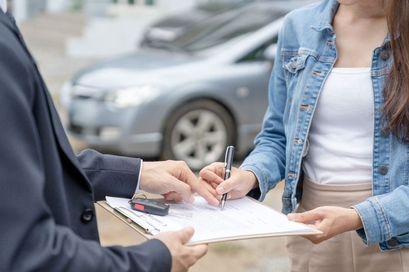 A handshake between a staff member and a customer in front of a car, or a smiling team member handing paperwork to a customer.